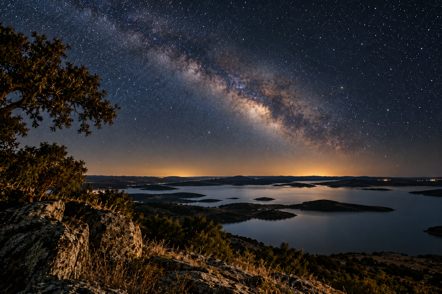 The Milky Way over Alqueva lake at night, seen from a rocky viewpoint above the water